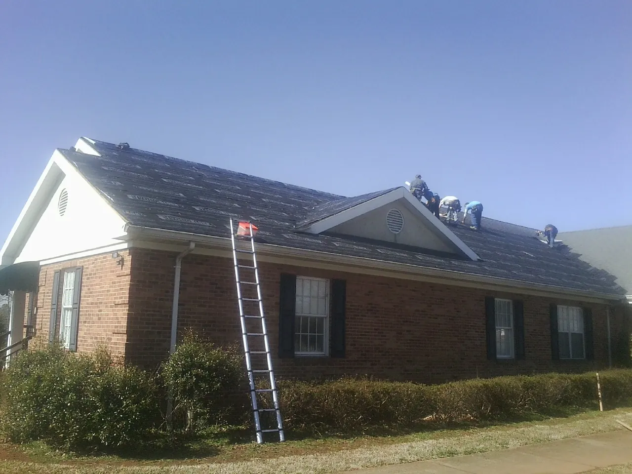 Crew tearing shingles off a brick ranch roof with a ladder set — Metal Roof Repair work by our crew in Moscow Mills