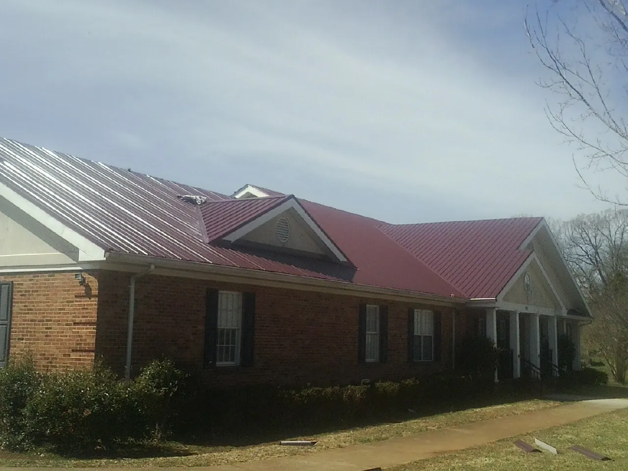 Red metal roof with gabled entries on a long brick building, from a Hail Damage Roof Repair job in Moscow Mills