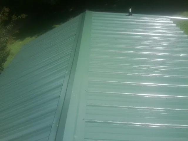 New green metal panels meeting at the ridge of a roof — Flat Roof Repair work by our crew in Moscow Mills