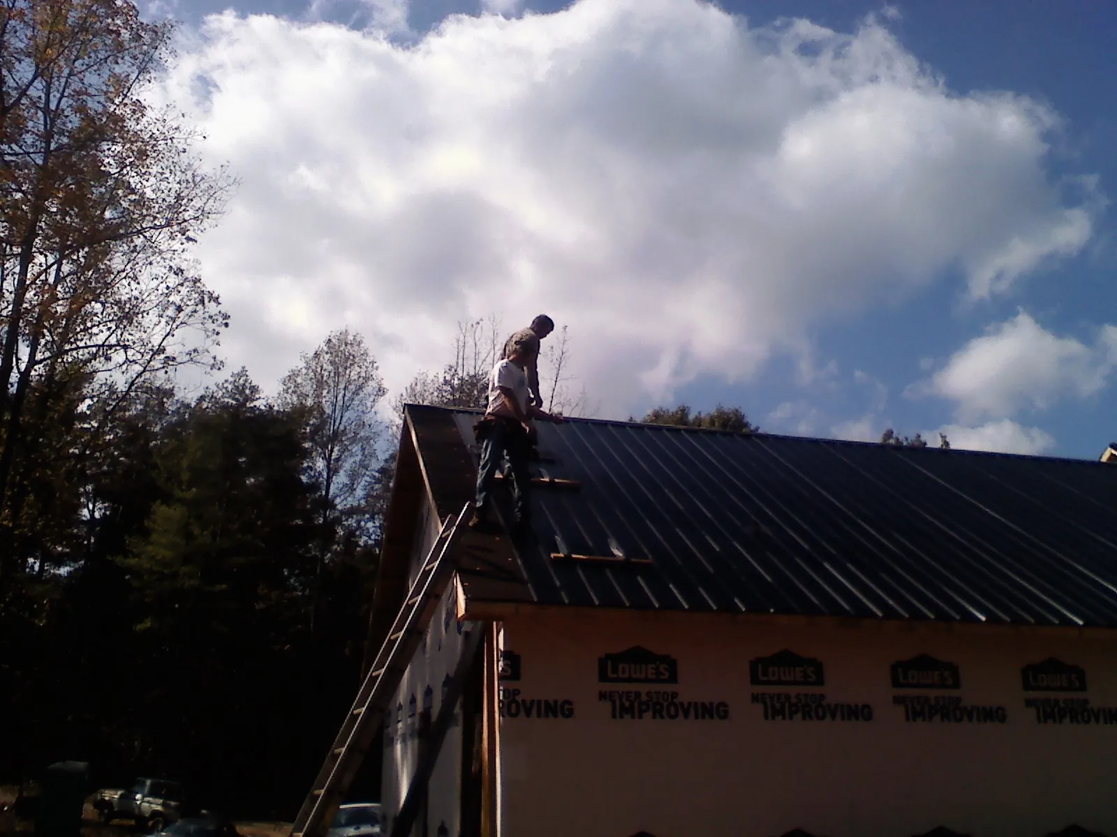 Roofer fastening dark metal panels high against a cloudy sky, from a Roof Inspection job in Moscow Mills
