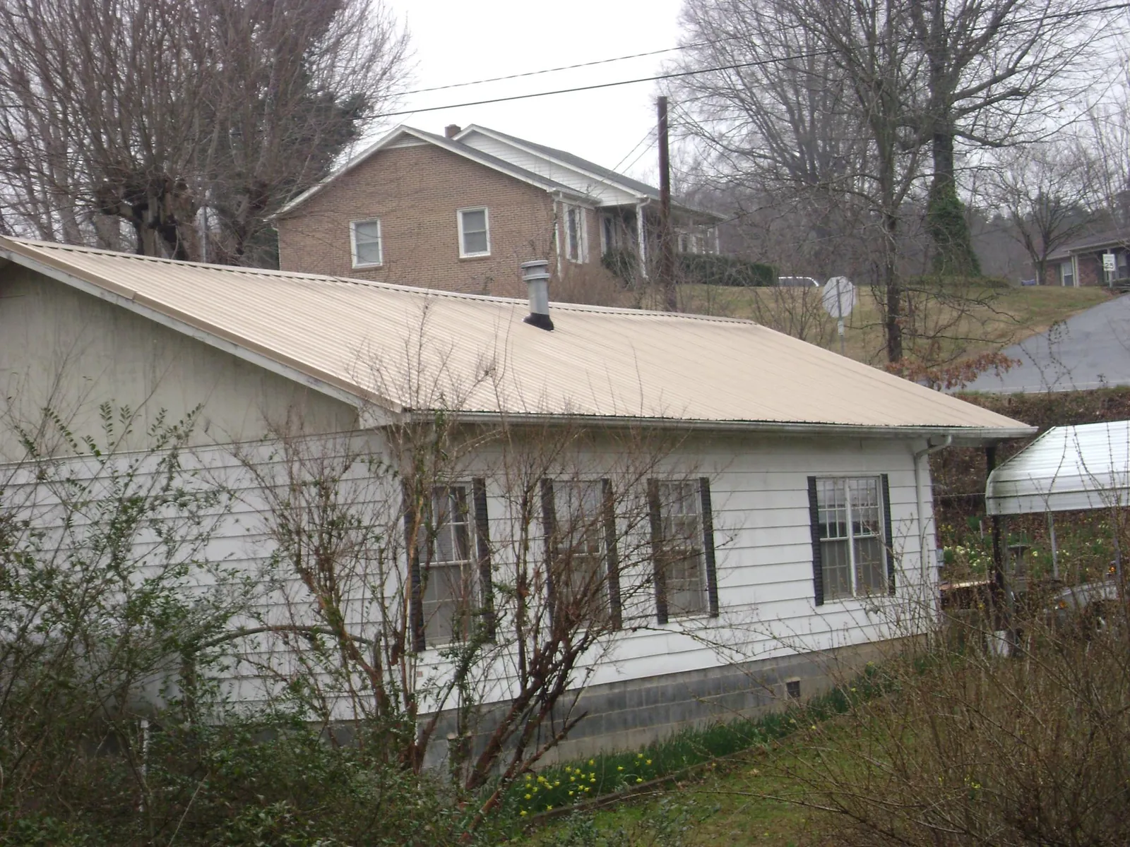 Tan metal roof on a white sided house set into a hillside — Commercial Roofing by Roofing Brothers in Moscow Mills