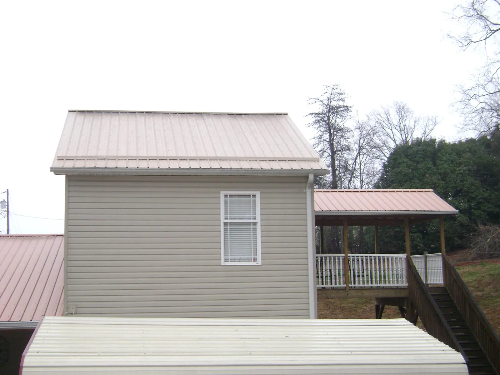 Tan metal roofs on a two story addition and attached porch, from a Roof Replacement job in Moscow Mills